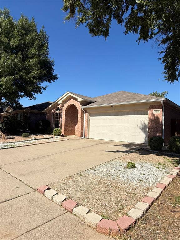 Brick exterior featuring a gabled roofline, arched entryway, and two-car garage with concrete driveway