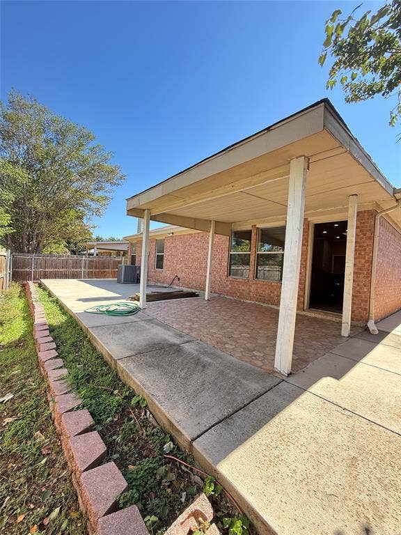 Covered patio with textured masonry flooring, brick exterior siding, and a decorative concrete block garden border