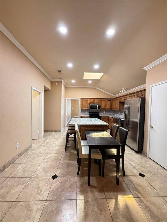 Kitchen featuring a central island with a stone-finish countertop, recessed lighting, vaulted ceiling with a skylight, tile flooring with decorative inserts, and wood cabinetry