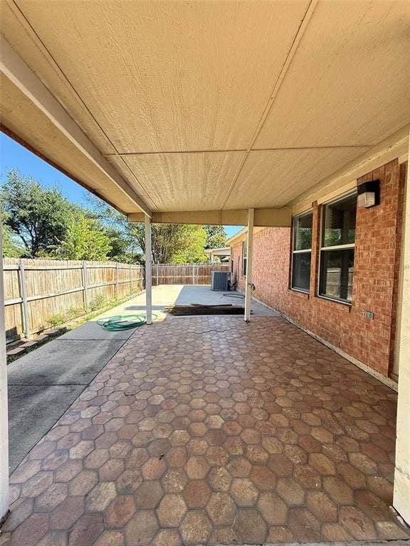 Covered rear patio featuring hexagon-patterned tile flooring, brick exterior masonry, and an attached wall-mounted light fixture