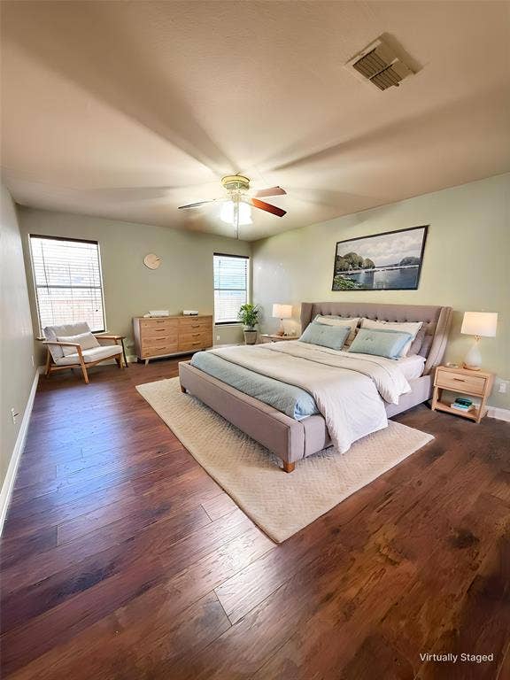 Spacious room featuring wood-finish flooring, dual windows with blinds, and a ceiling fan with integrated lighting