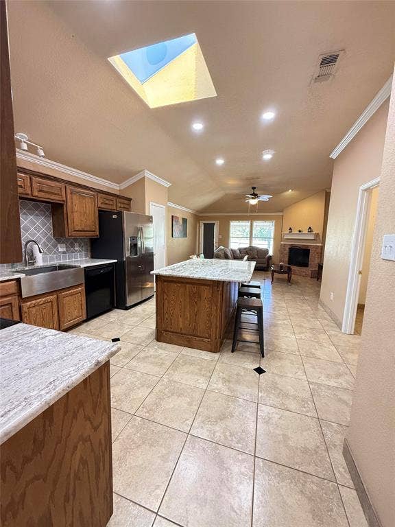 Kitchen featuring a central island with stone countertop, stainless steel apron-front sink, patterned tile backsplash, recessed lighting, and a vaulted ceiling with skylight