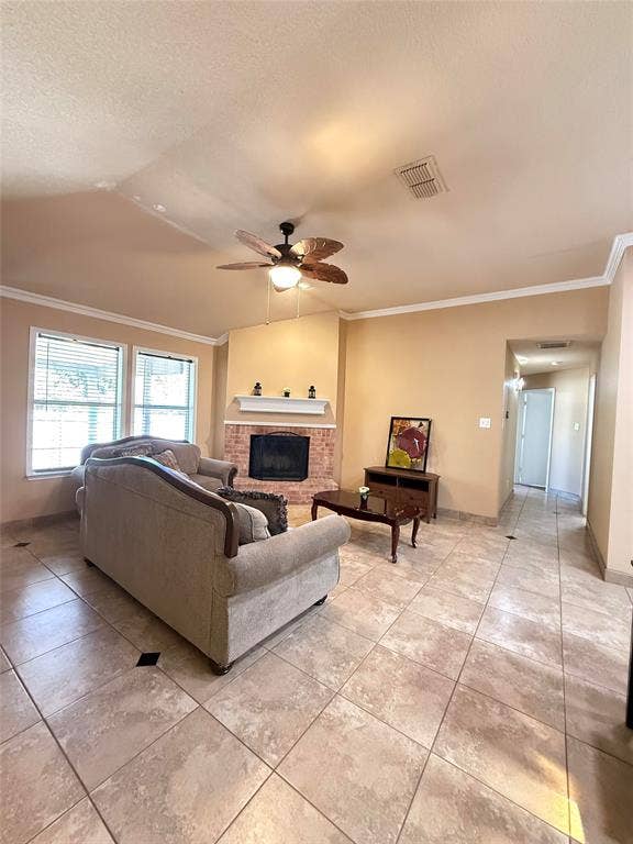 Vaulted ceilings with crown molding, brick fireplace with a painted wood mantel, tile flooring with decorative inlay accents, and a ceiling fan with integrated lighting