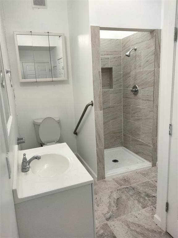 Bathroom featuring a white vanity with an integrated sink, stone-finish floor tiling, a walk-in shower with neutral wall tiling and a built-in shower niche, and a wall-mounted medicine cabinet