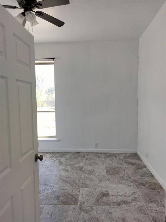 Interior space featuring neutral wall tones, large-format tile flooring with natural stone-pattern detailing, a vertical window with minimal casing, and a ceiling-mounted fan with integrated lighting