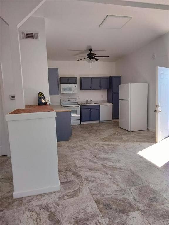Kitchen featuring blue cabinetry, stone-finish tile flooring, integrated white appliances, and a ceiling-mounted fan