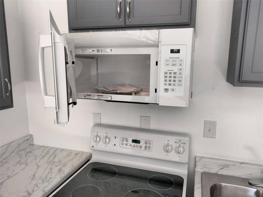 Built-in over-the-range microwave, white electric range with four-burner cooktop, gray shaker-style cabinetry, and stone-finish laminate countertops