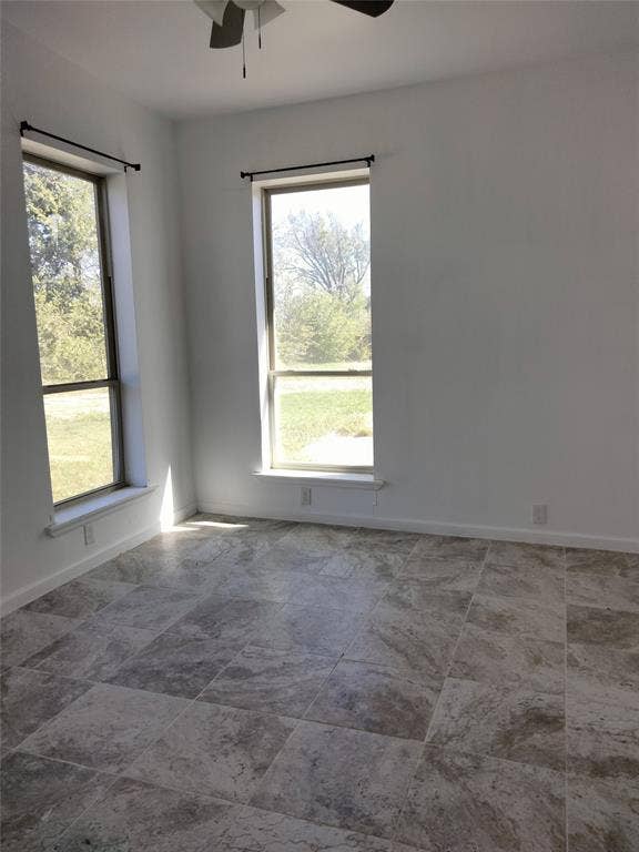 Neutral-toned stone tile flooring, dual full-height windows, and ceiling fan fixture