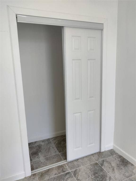 Closet featuring a white six-panel sliding door and stone-finish tile flooring