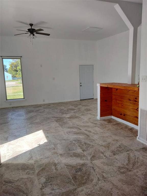 Vaulted ceilings featuring a ceiling fan, stone-patterned tile flooring, and a wood-paneled built-in counter