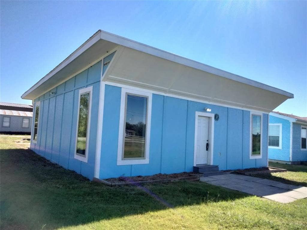 Single-story exterior featuring vertical panel siding, a cantilevered roofline, tall rectangular windows, and a concrete pathway