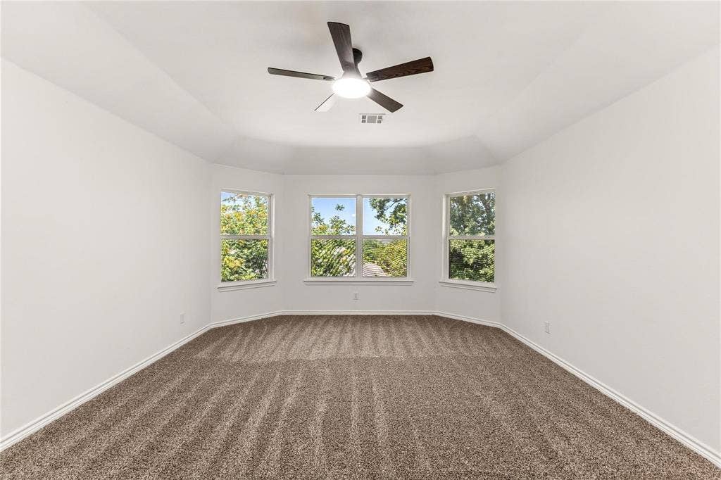 Room featuring a tray ceiling, triple-window bay configuration, wall-to-wall carpeting, and a central ceiling fan with an integrated light fixture