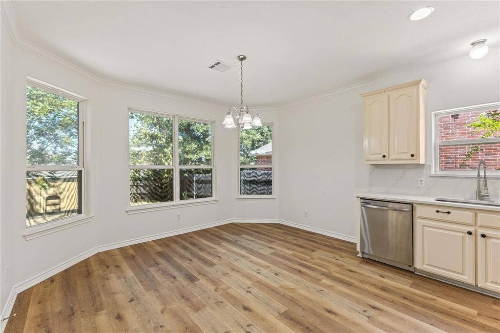 Wood-finish flooring, bay windows with natural lighting, off-white cabinetry, stainless steel dishwasher, and hanging chandelier