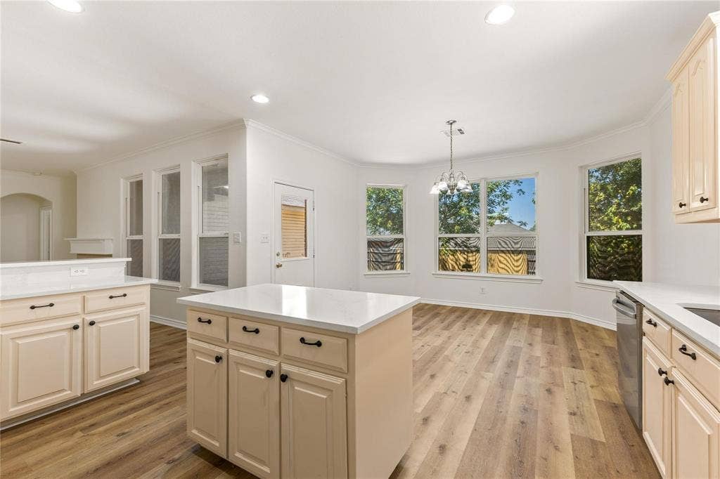 Kitchen featuring a central island with a solid-surface countertop, wood-finish flooring, recessed lighting, and a multi-paneled windowed breakfast area