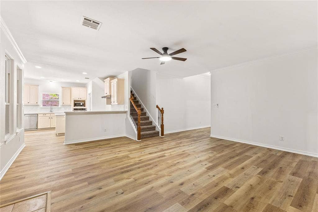 Open-concept interior featuring wood-finish flooring, a ceiling fan with integrated lighting, and a staircase with a wooden handrail and metal balusters