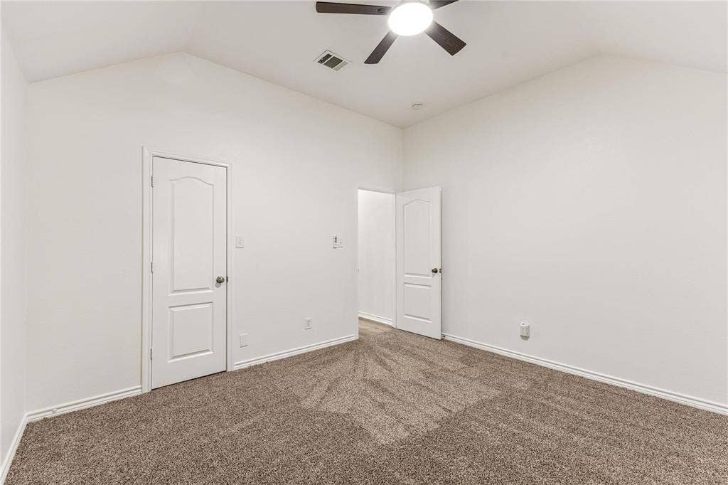 Vaulted ceiling featuring a central lighted ceiling fan, neutral wall-to-wall carpeting, and two interior doors with arched-panel detailing