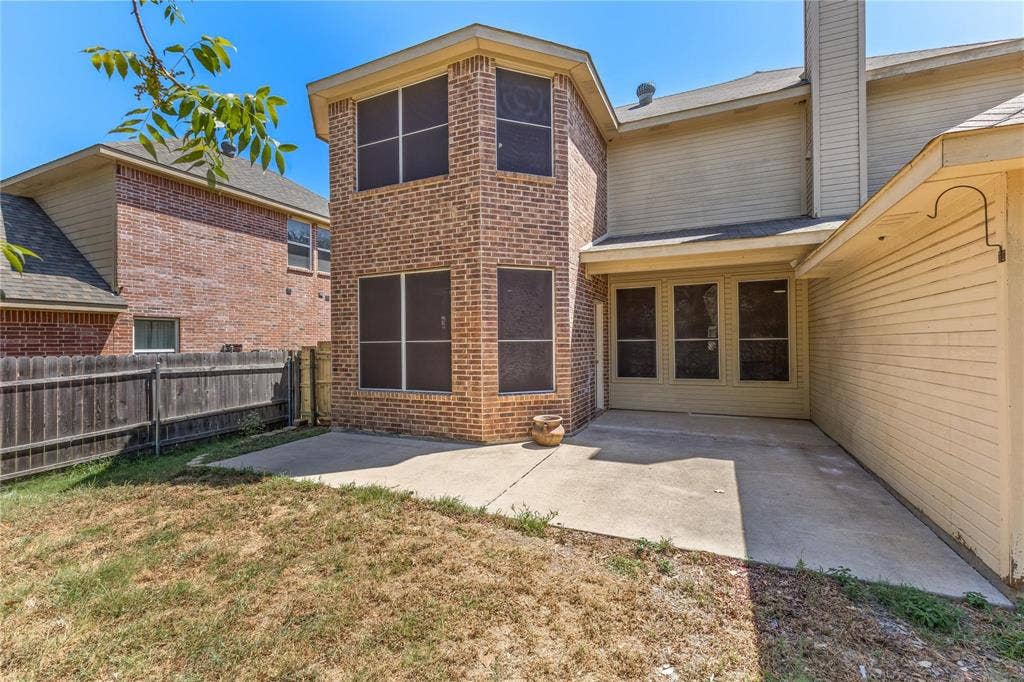 Rear exterior featuring brick masonry, horizontal siding, a concrete patio, and a wood privacy fence