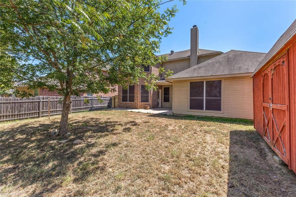 Rear yard featuring a wood fence, mature tree, concrete patio, and detached storage structure