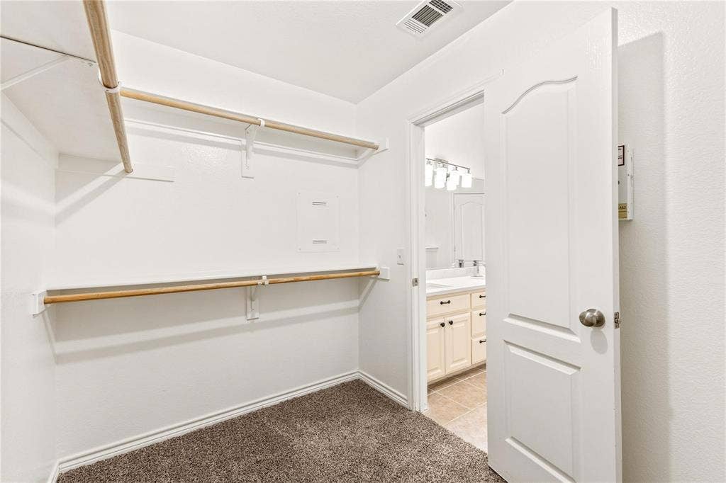 Walk-in closet featuring tiered wood shelving and rods, neutral carpeting, and a raised-panel interior door