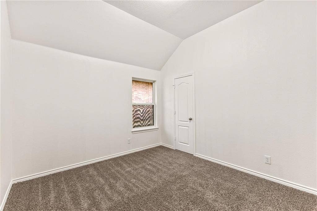 Room featuring vaulted ceilings, neutral-toned carpeting, and a single-panel interior door