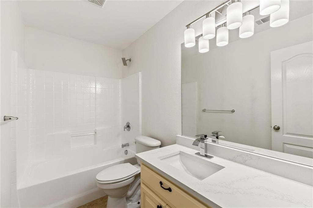 Bathroom featuring a vanity with a white composite countertop, an integrated rectangular sink, a multi-bulb light fixture, a large wall-mounted mirror, and a tub-shower combination with tiled surround