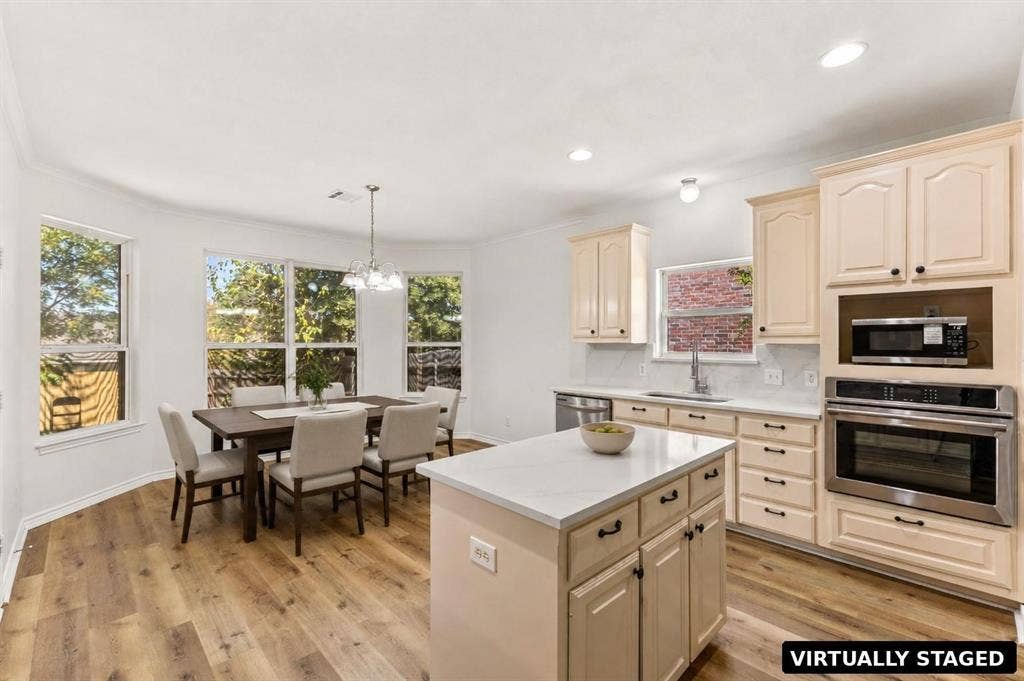 Kitchen featuring light-toned cabinetry, stone-surface countertops, center island, built-in stainless steel oven and microwave, and wood-finish flooring