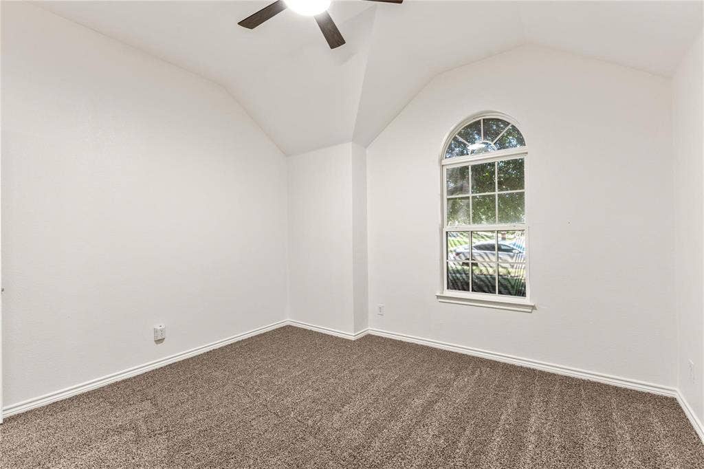 Vaulted ceiling featuring a central lighted ceiling fan, arched window, and neutral wall-to-wall carpeting