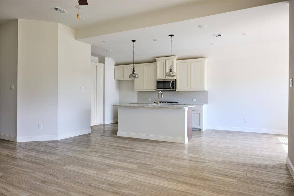 Kitchen featuring light-toned cabinetry, a stone-surfaced island with a sink, recessed lighting, dual pendant fixtures, and wood-finish flooring