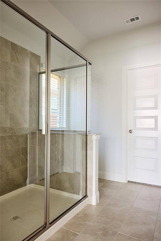 Walk-in shower featuring a glass enclosure with a metal frame, neutral-toned tile surround, and a four-panel door