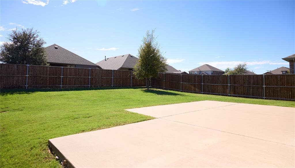 Backyard featuring a concrete patio, sodded lawn, perimeter wood fencing, and an established tree