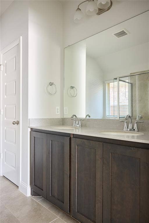 Double vanity featuring dark-stained wood cabinetry, stone-finish countertops, dual undermount sinks, and a full-width wall mirror