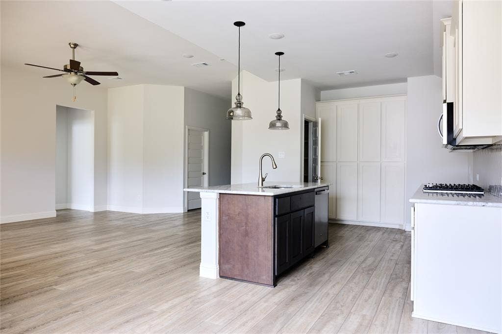 Kitchen featuring a center island with a stone countertop, built-in cabinetry, wood-finish flooring, dual pendant lighting, and a stainless steel sink fixture