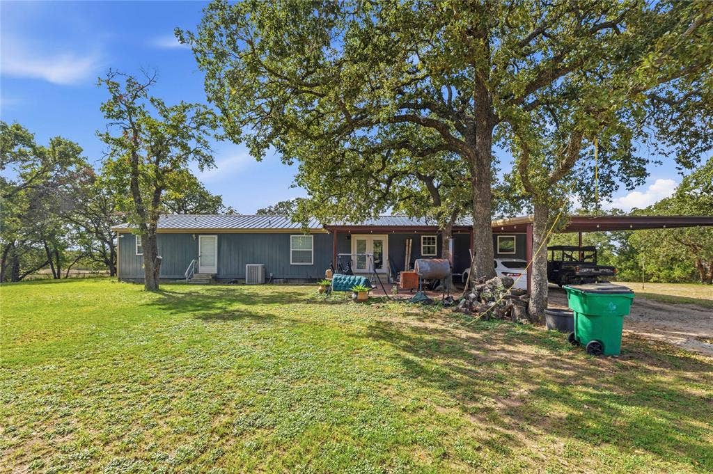 5540 County Road 334, Blanket, TX 76432 Exterior featuring metal roof, vertical siding, attached carport, French doors, and mature shade trees