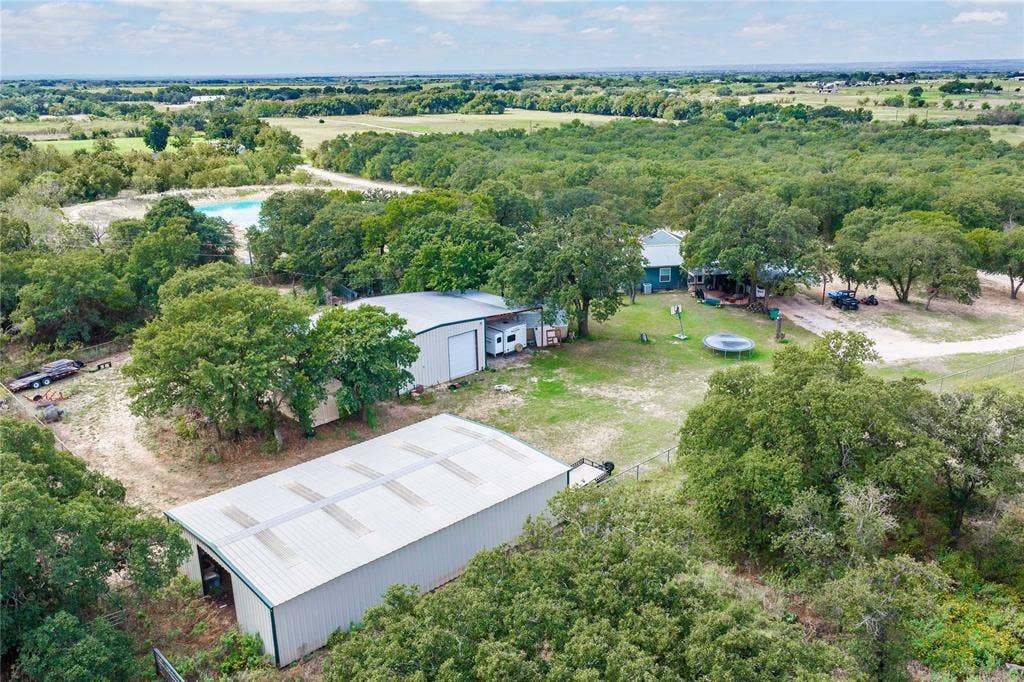 5540 County Road 334, Blanket, TX 76432 Expansive rural acreage featuring two detached metal-sided workshops, mature tree canopy, and gravel driveways