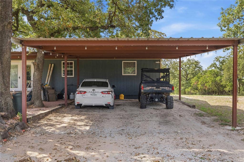 5540 County Road 334, Blanket, TX 76432 Metal-frame carport with integrated lighting, finished exterior siding, and a gravel driveway surface