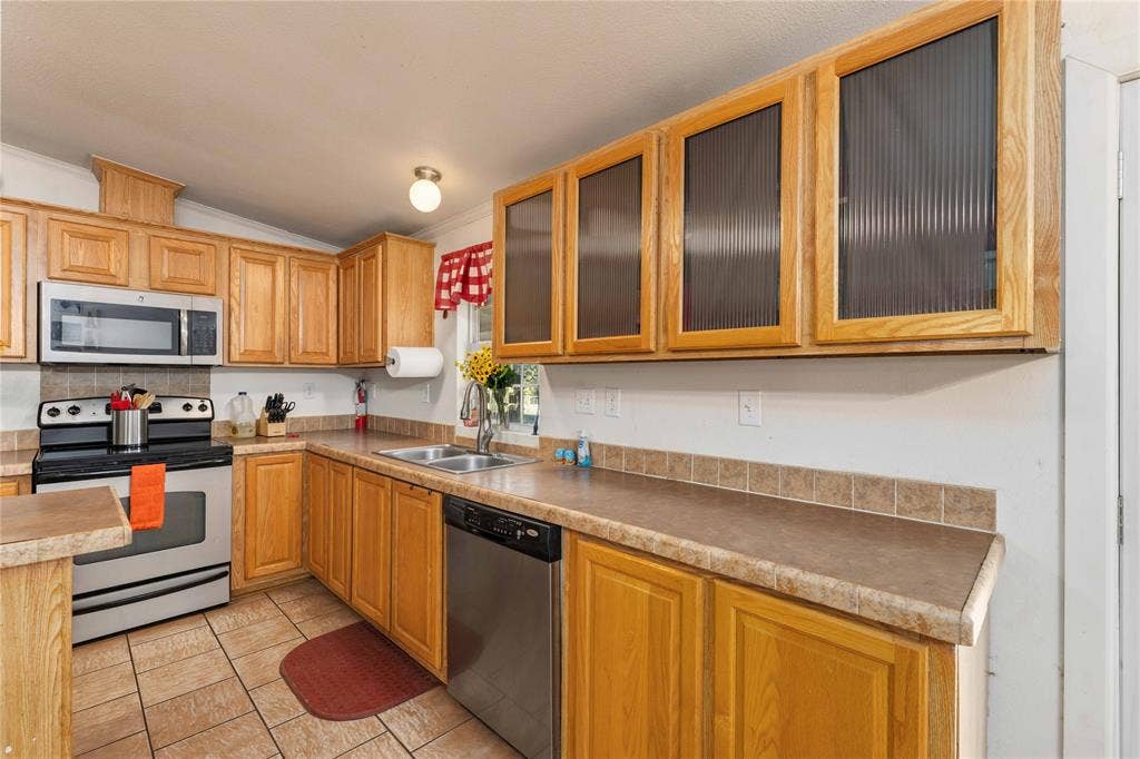 5540 County Road 334, Blanket, TX 76432 Kitchen featuring natural wood cabinetry with upper glass-panel doors, neutral stone-finish countertops, tile backsplash, and stainless steel appliances