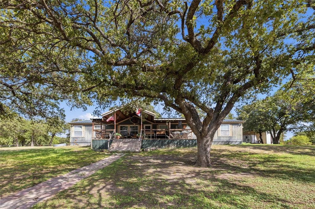 5540 County Road 334, Blanket, TX 76432 Exterior facade featuring a covered front porch, metal roofing, mature oak trees, and a stone walkway