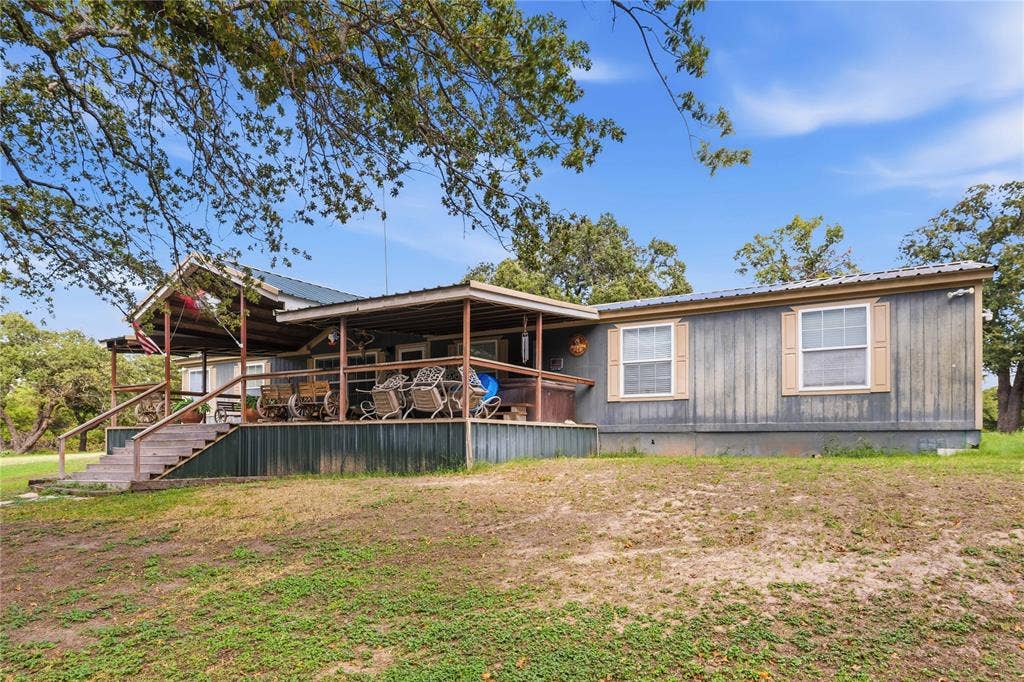 5540 County Road 334, Blanket, TX 76432 Exterior featuring vertical panel siding, a metal roof, and an expansive covered porch with wooden stairs and railing