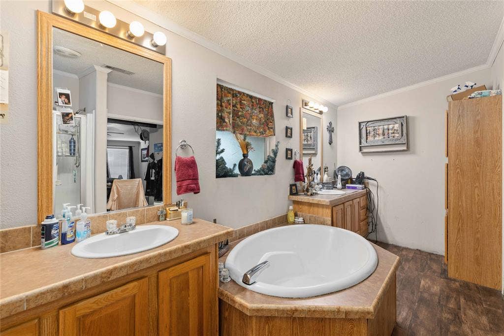 5540 County Road 334, Blanket, TX 76432 Bathroom featuring dual wood-finish cabinetry, tile-surround drop-in soaking tub, wood-finish flooring, and wall-mounted vanity lighting