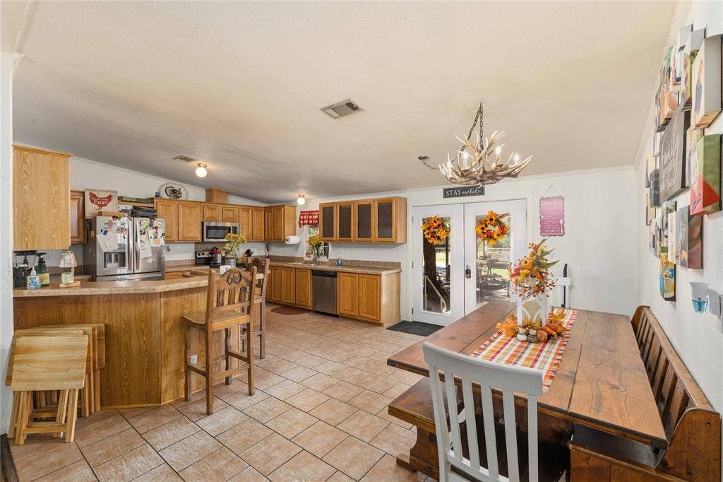 5540 County Road 334, Blanket, TX 76432 Kitchen featuring wood cabinetry, stainless steel appliances, breakfast bar, tile flooring, and a decorative chandelier