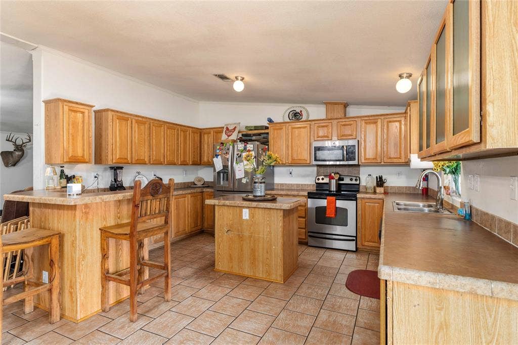 5540 County Road 334, Blanket, TX 76432 Kitchen featuring light-finish wood cabinetry, a central island, stainless steel appliances, ceramic tile flooring, and a breakfast bar