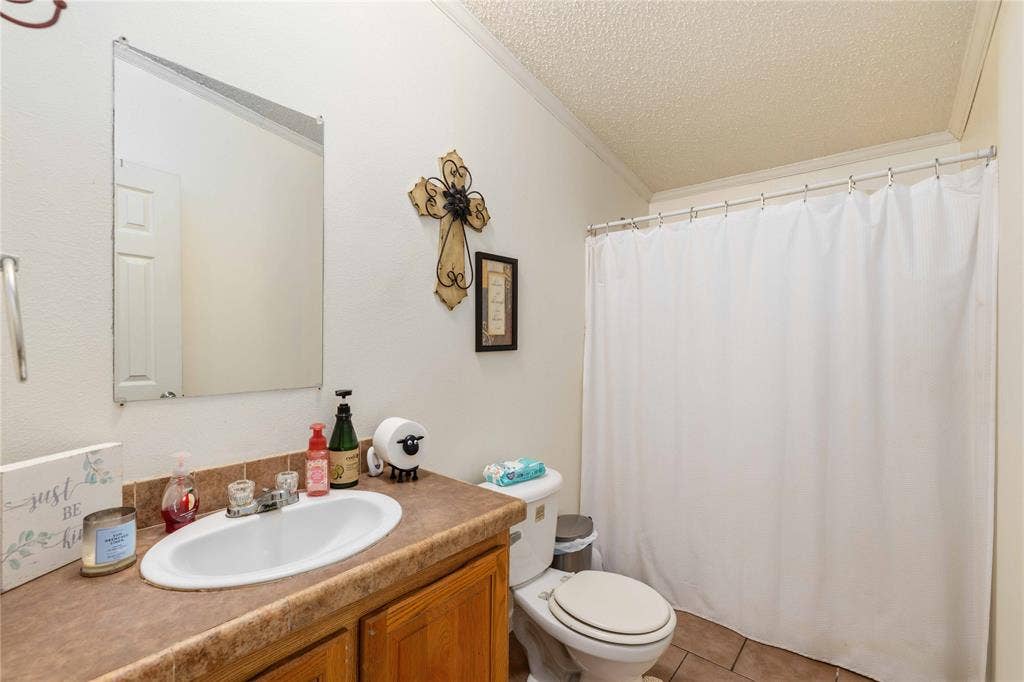 5540 County Road 334, Blanket, TX 76432 Bathroom featuring an integrated vanity with an oval sink, solid-surface countertop, wood-finish cabinetry, frameless wall-mounted mirror, and tile flooring