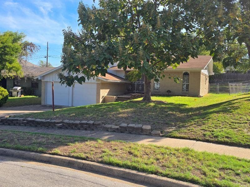 7716 Ryanridge Drive, Dallas, TX 75232 Single-story brick exterior featuring an attached two-car garage, arched windows, concrete steps, and a decorative metal storm door