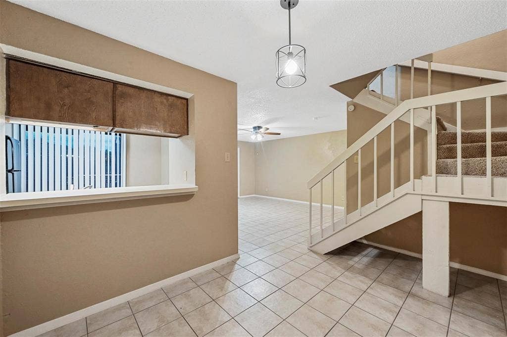 14800 Enterprise Drive, #22D, Farmers Branch, TX 75234 Interior area featuring ceramic tile flooring, a pass-through window with built-in wooden cabinetry, a geometric pendant light fixture, and a staircase with a white wooden railing