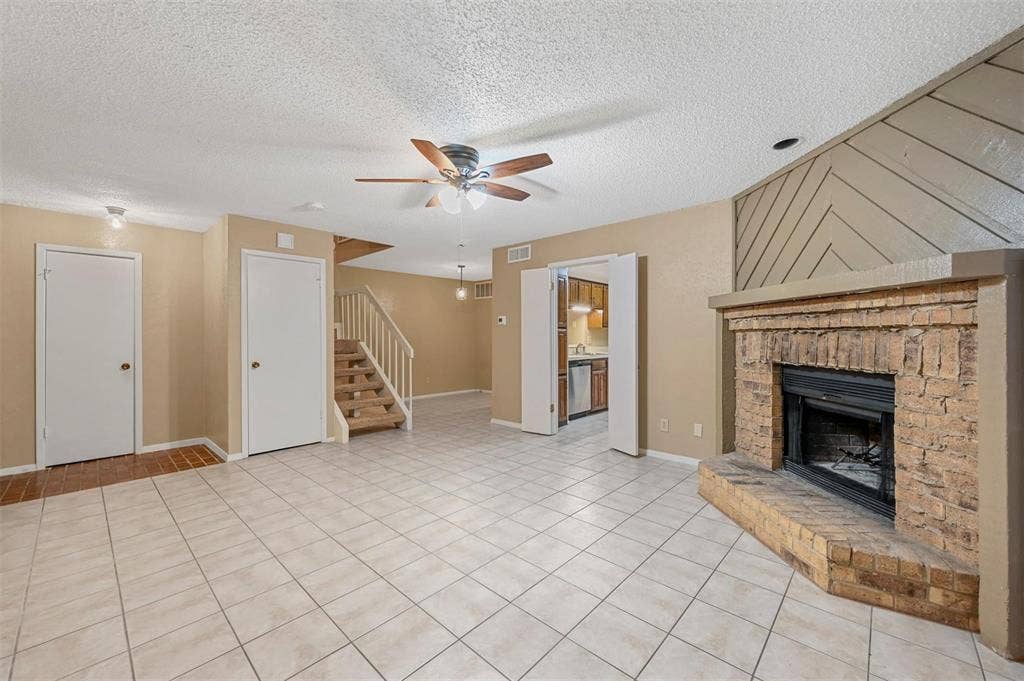 14800 Enterprise Drive, #22D, Farmers Branch, TX 75234 Interior area featuring tile flooring, a floor-to-ceiling brick fireplace with an elevated hearth, a decorative wood-panel accent wall, and a staircase with a wooden balustrade