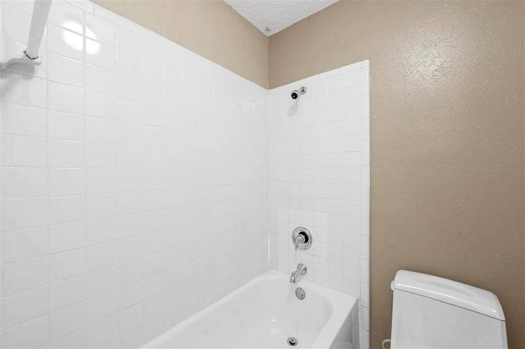 14800 Enterprise Drive, #22D, Farmers Branch, TX 75234 Bathtub with white tiled surround, chrome shower head and faucet hardware, and standard toilet