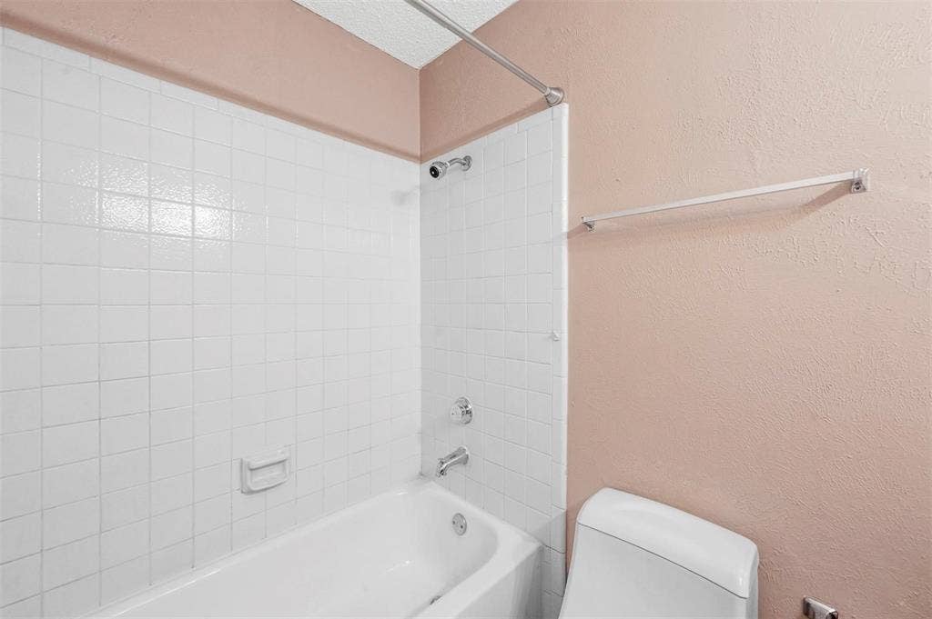 14800 Enterprise Drive, #22D, Farmers Branch, TX 75234 Bathtub enclosure featuring white square tile wall surrounds, a built-in recessed soap niche, chrome plumbing fixtures, a metal curtain rod, and a wall-mounted towel bar