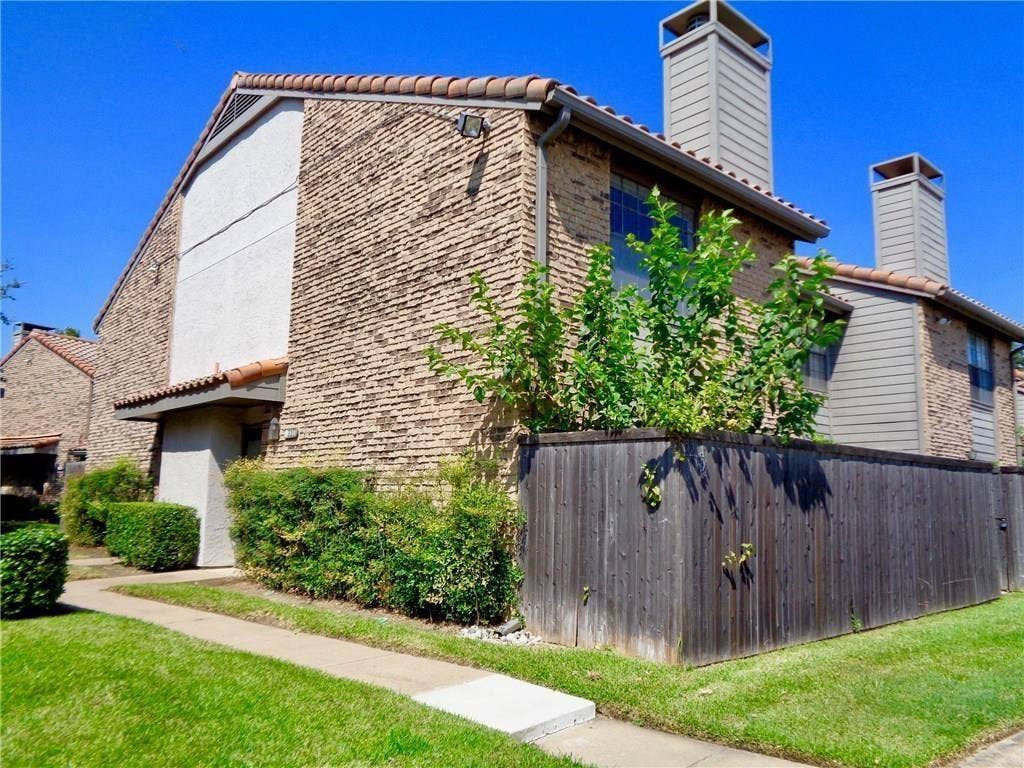 14800 Enterprise Drive, #22D, Farmers Branch, TX 75234 Multi-story exterior featuring textured brick and stucco siding, a tiled roof, dual chimneys, and a private wooden fence