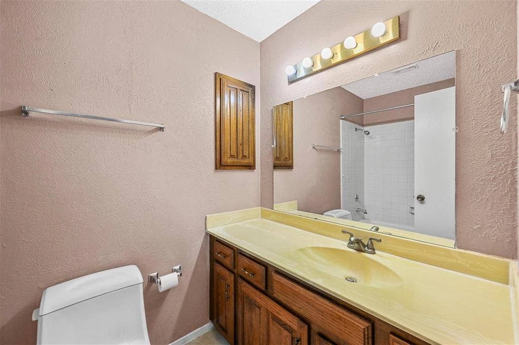 14800 Enterprise Drive, #22D, Farmers Branch, TX 75234 Bathroom featuring a vanity with integrated sink, wood-finish cabinetry, a large wall-mounted mirror, overhead five-bulb lighting, and a white tiled shower surround