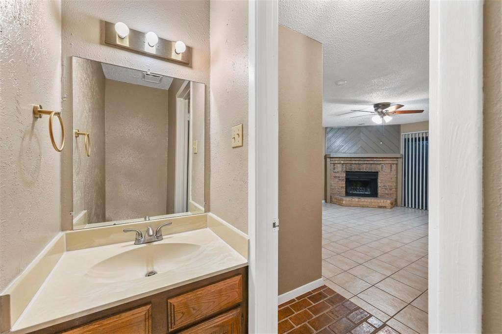 14800 Enterprise Drive, #22D, Farmers Branch, TX 75234 Bathroom featuring a wooden vanity, integrated countertop with sink, and three-light wall fixture